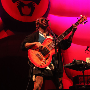 A guitarist performing on stage, bathed in vibrant pink and purple lights