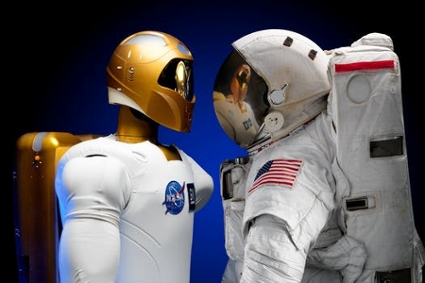 A humanoid robot in a NASA T-shirt standing face-to-face with a human astronaut