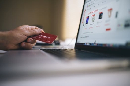 A hand holding a credit card in front of an open laptop screen, suggesting an online purchase