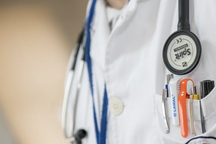 Close-up of a doctor in a white coat, with a stethoscope draped around his neck and several pens tucked into his pocket