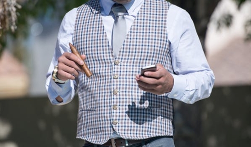 A well-dressed individual in business clothing with a pen in one hand and a phone in the other