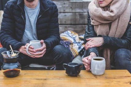A man and a lady enjoying coffee, sitting close with cups in hand
