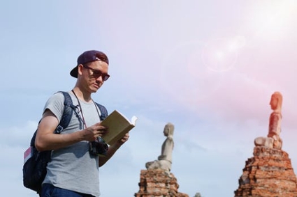 A man stands outdoors reading a book in front of a row of monuments