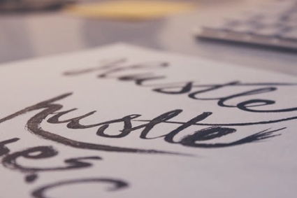 The word “hustle” written in cursive on a white sheet of paper