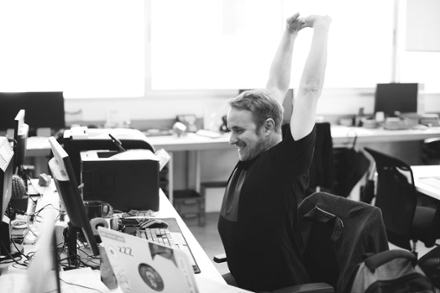 A man smiling as he stretches his arms, sitting on his work desk
