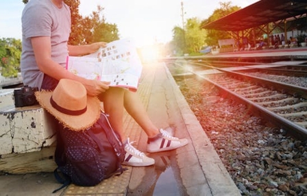 Woman sitting beside train tracks with the sun shining brightly in the background