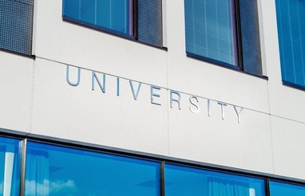The exterior of a large, white university building with the word 'University' engraved