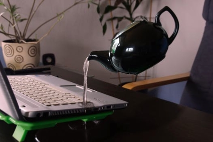 Stream of water poured from a kettle onto a laptop