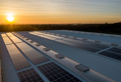Multiple rows of solar panels stretch across a field, silhouetted against a colorful sunset sky