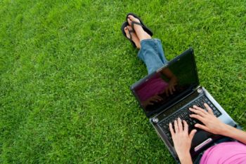 A person relaxing on a green lawn while working on the laptop